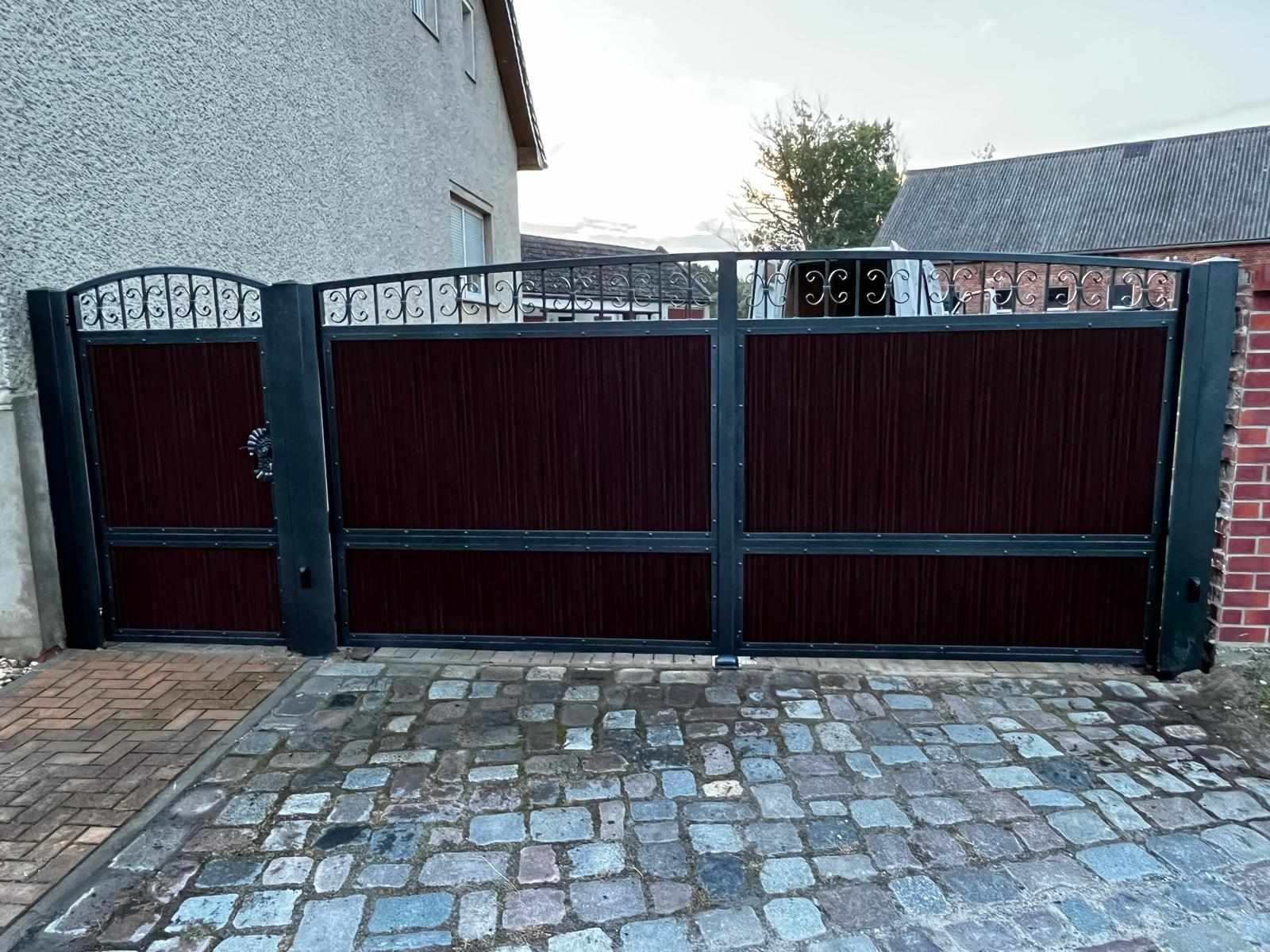 Nowoczesna brama wjazdowa z ciemnego drewna i ozdobnymi elementami metalowymi, ułożona na kostce brukowej w odcieniach szarości.