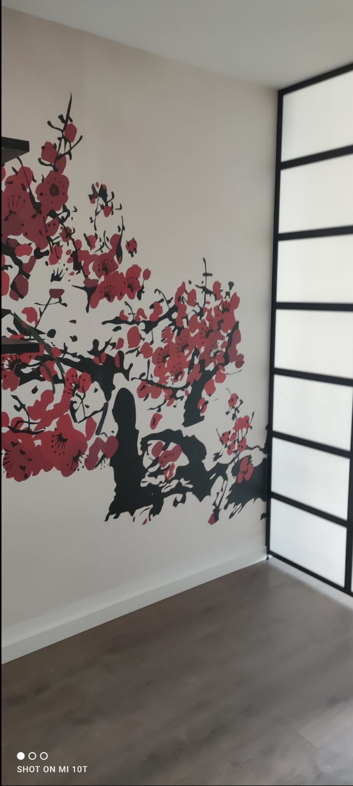 Ściana z dekoracyjnym malunkiem kwitnącej wiśni w kolorach czerwieni i czerni, uzupełniona o przesuwne drzwi w stylu japońskim z czarną ramą i mlecznym szkłem.