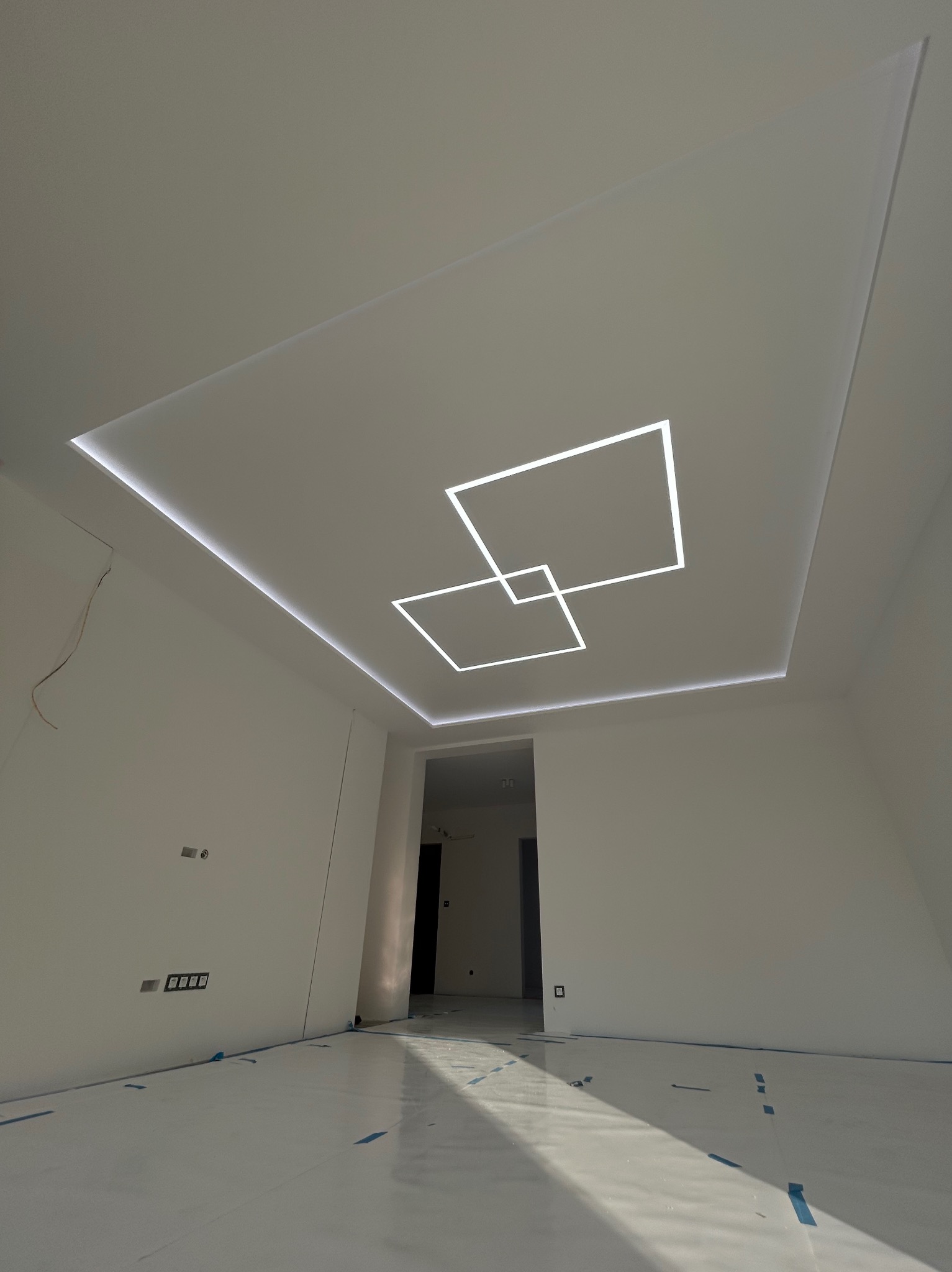 Nowoczesny sufit podwieszany z oświetleniem LED w kształcie kwadratów, białe ściany, zabezpieczona podłoga. Minimalistyczny design wnętrza.