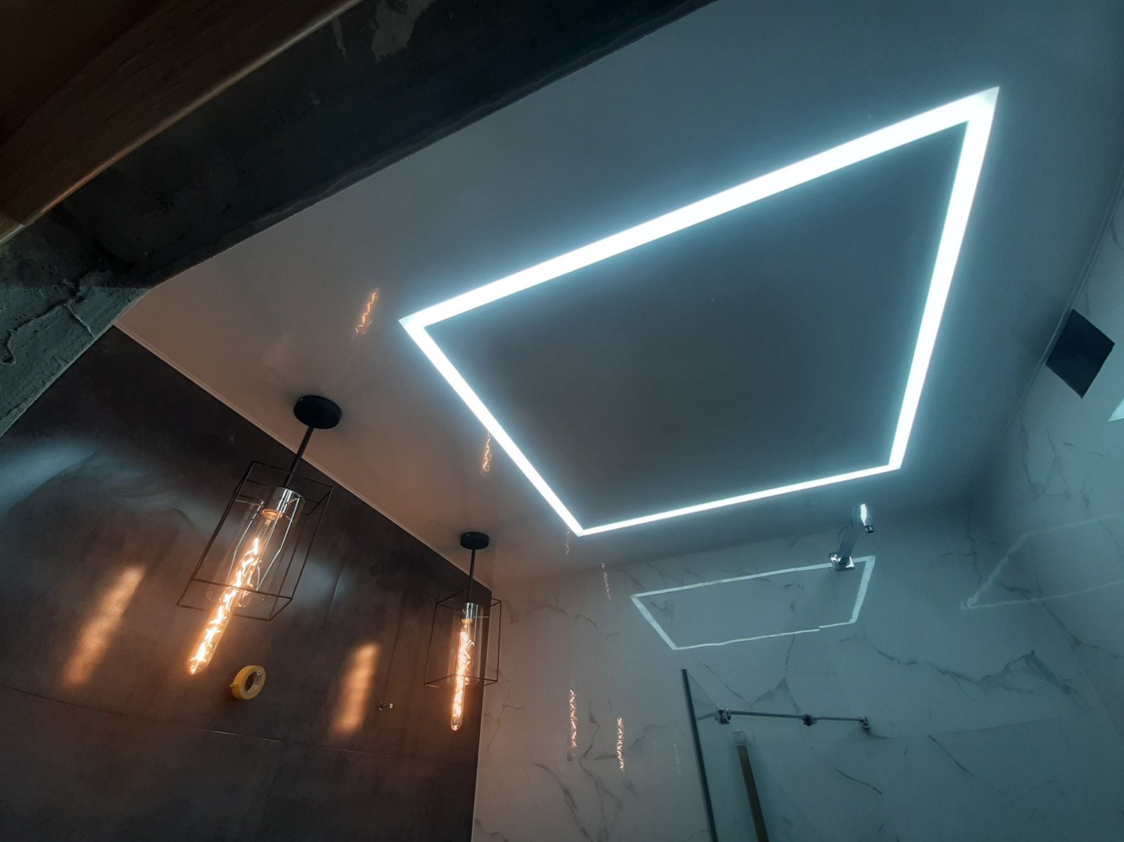 Nowoczesna łazienka z sufitem napinanym, oświetleniem LED w kształcie kwadratu i designerskimi lampami wiszącymi. Marmurowe płytki na ścianach.