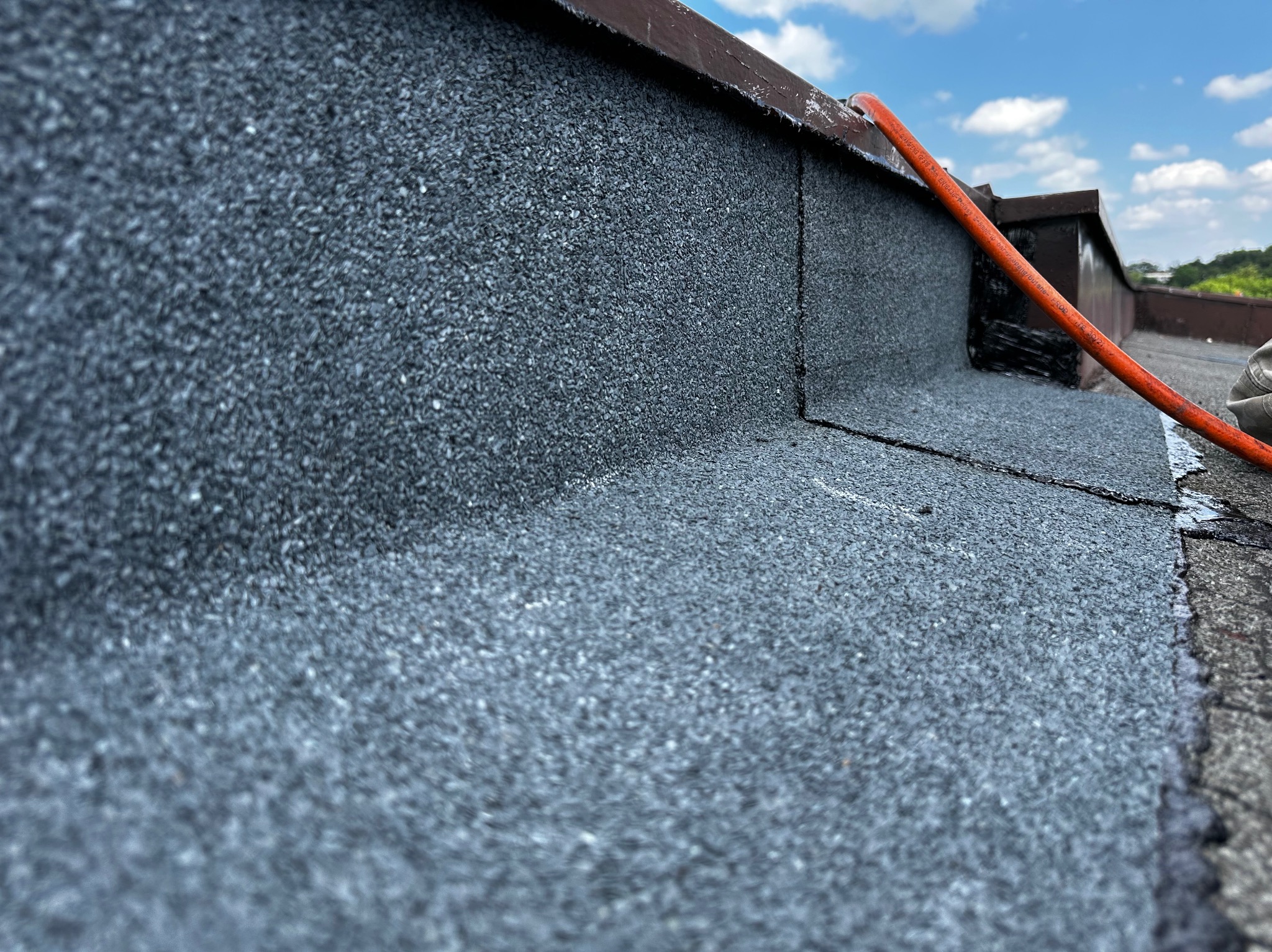 Szczegółowe ujęcie nowo położonej papy na dachu z widocznym przewodem pomarańczowym i fragmentem obróbki blacharskiej