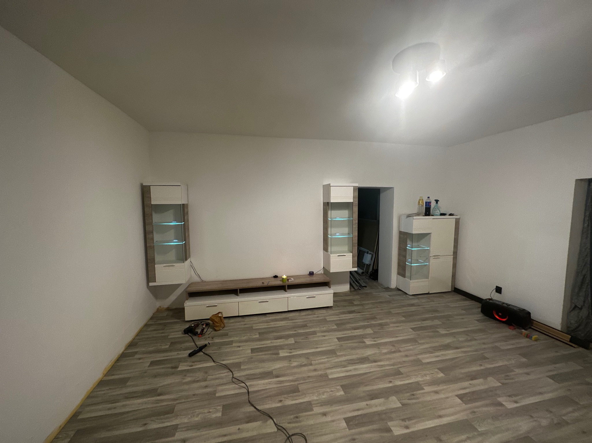 Pokój z nowymi panelami podłogowymi w odcieniach szarości, meblami w kolorze białym i beżowym oraz widocznymi narzędziami do montażu podłogi.