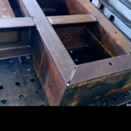 Metalowa konstrukcja spawana na stole spawalniczym z widocznymi spawami i oznaczeniami na elementach. Detal z bliska, ukazujący precyzję wykonania.