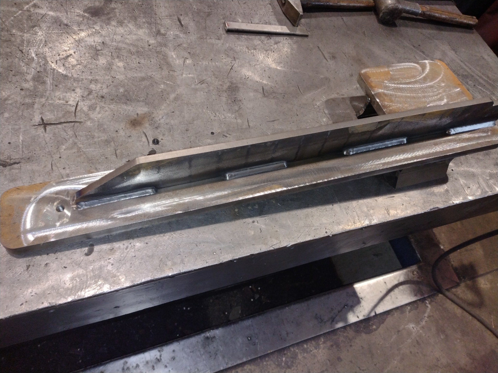 Metalowy element po spawaniu, widoczne spawy na metalowej konstrukcji w Garbatce-Letnisko, na tle warsztatowego stołu.