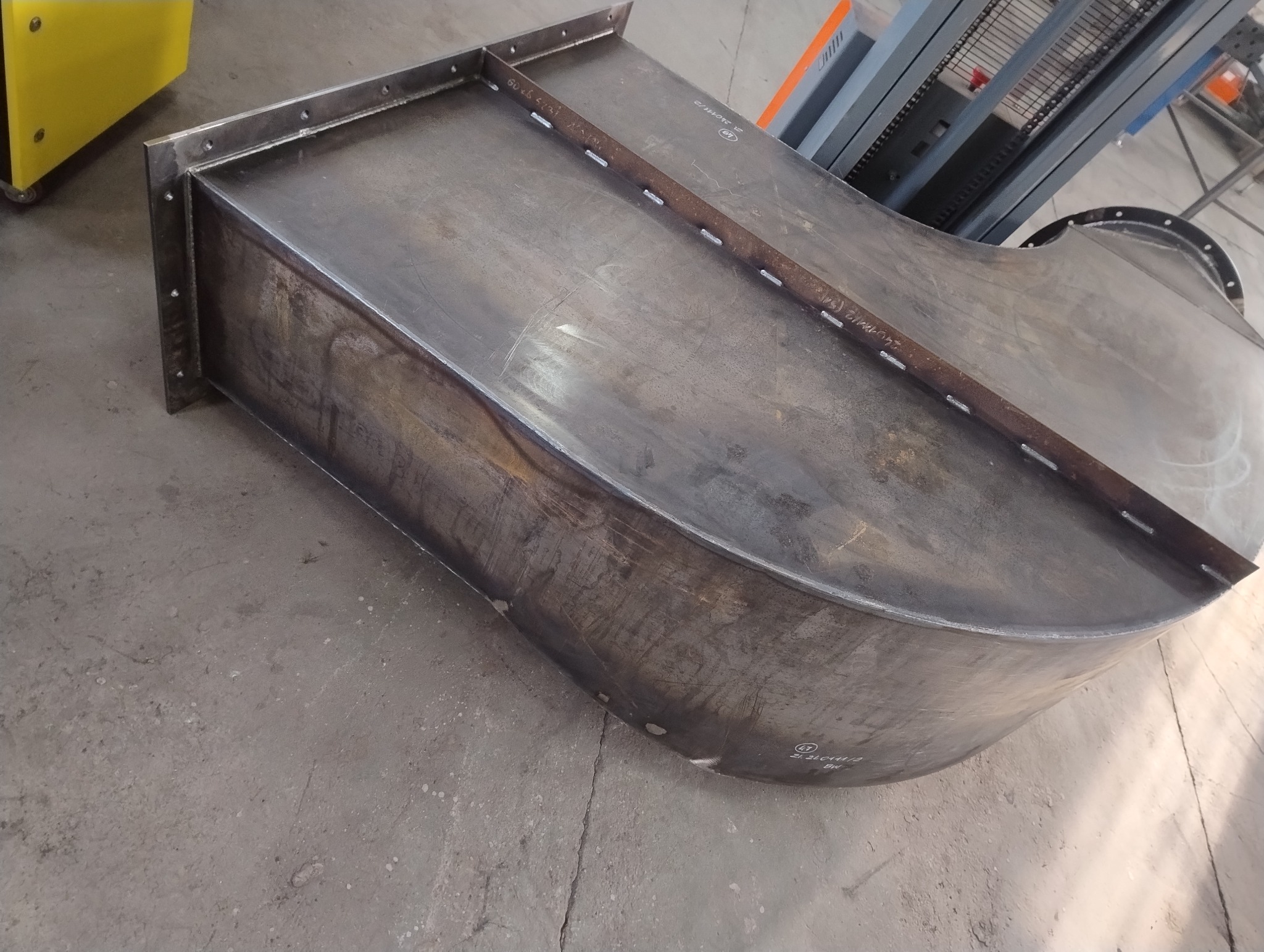 Spawana konstrukcja stalowa z elementami mocującymi i widocznymi śladami po spawaniu, leżąca na betonowej podłodze w warsztacie.