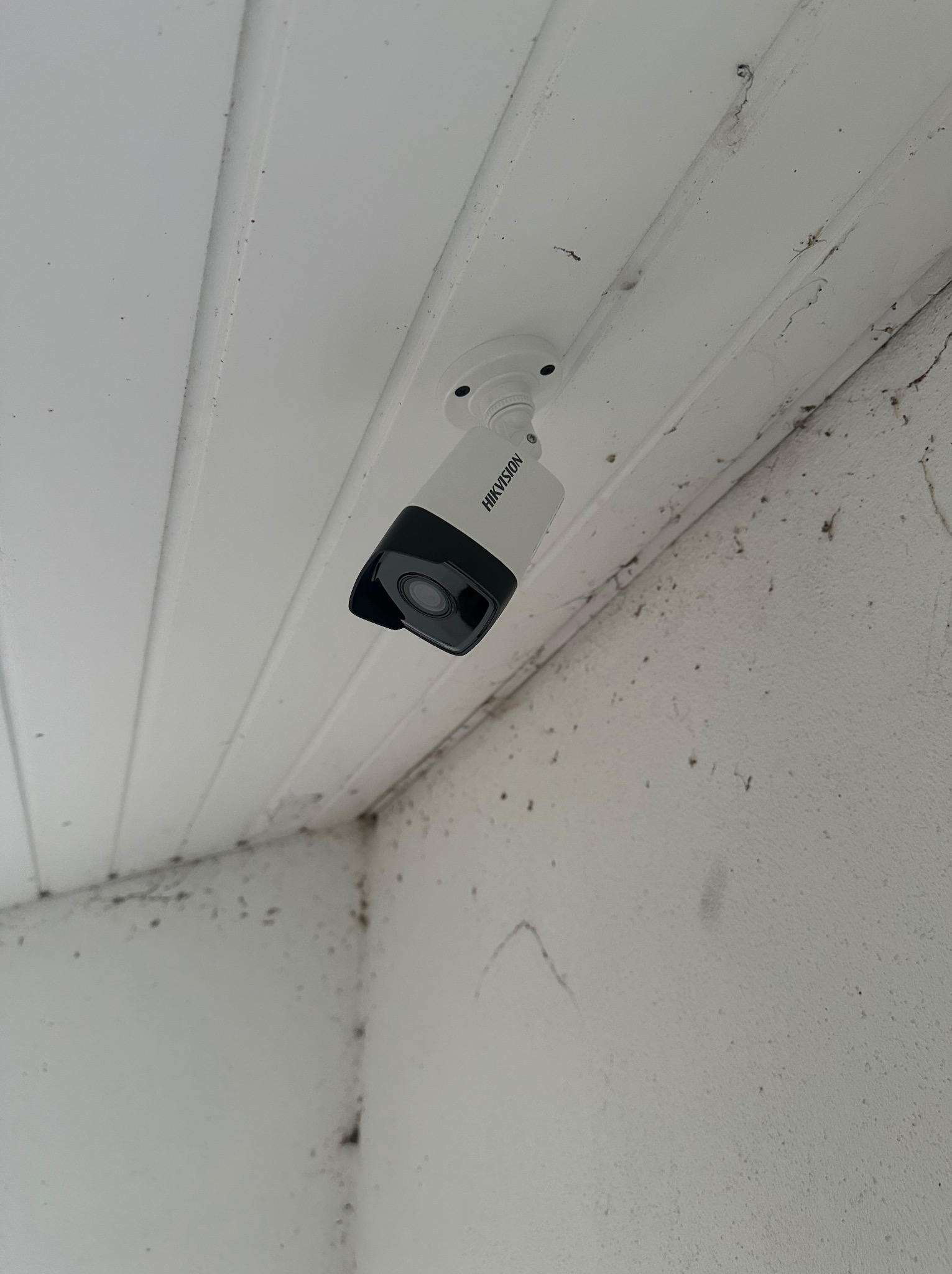 Kamera monitoringu Hikvision zamontowana pod sufitem z boazerii, widoczne zabrudzenia na suficie i ścianie.