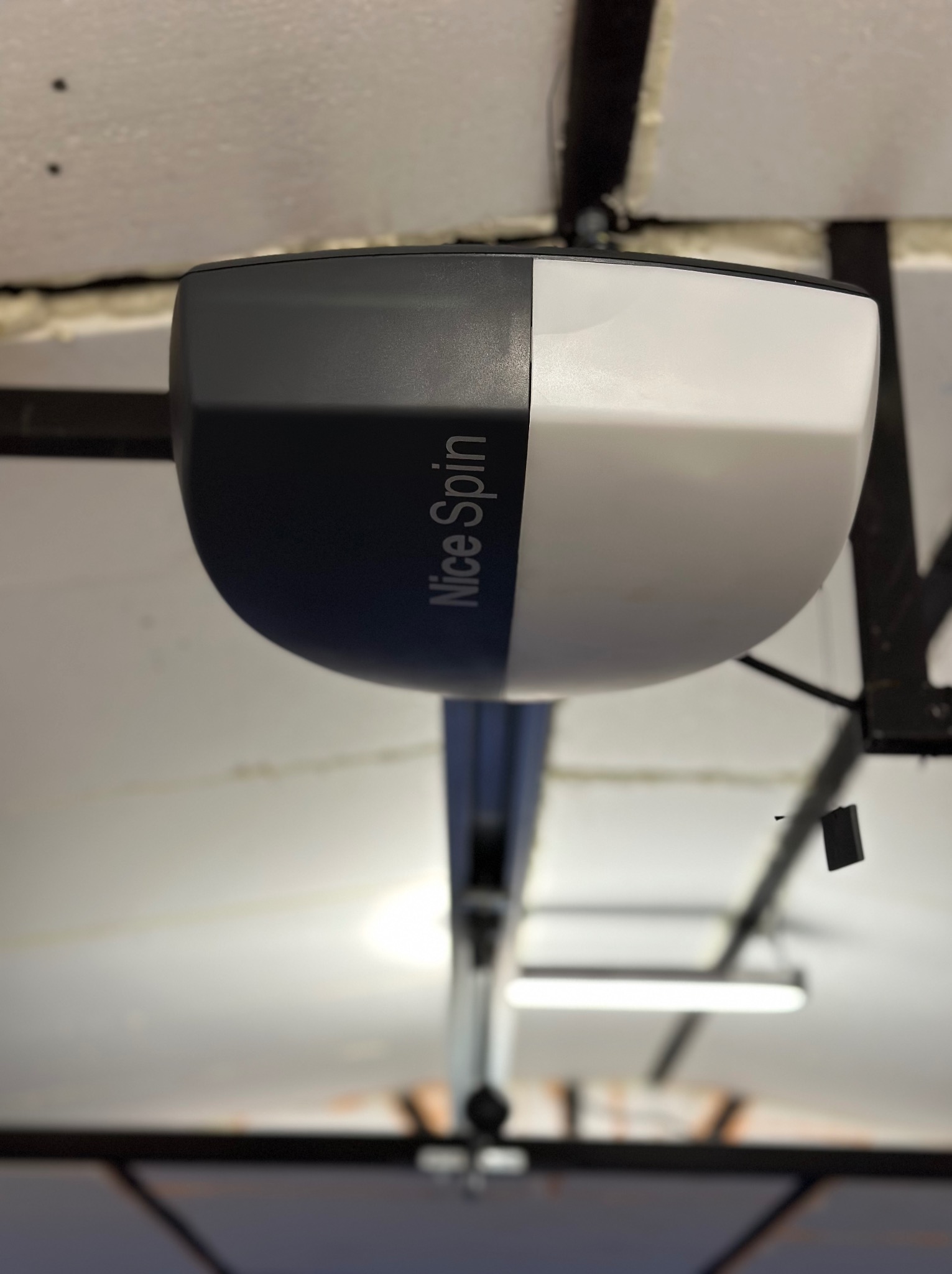 Zamontowany napęd do bramy garażowej Nice Spin, widok od dołu, z widoczną szyną prowadzącą i elementami konstrukcyjnymi sufitu garażu.