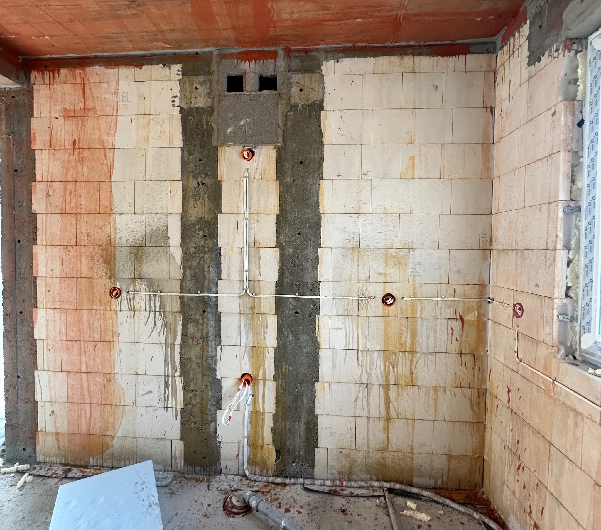 Instalacja elektryczna w trakcie montażu w surowym wnętrzu. Widoczne przewody, puszki elektryczne w ścianie z betonu komórkowego. Etap prac przed tynkowaniem.