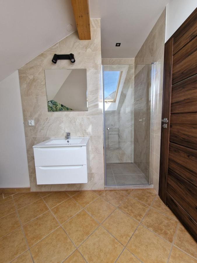 Nowoczesna łazienka na poddaszu z kabiną prysznicową, białym zlewem i brązową drewnianą podłogą.