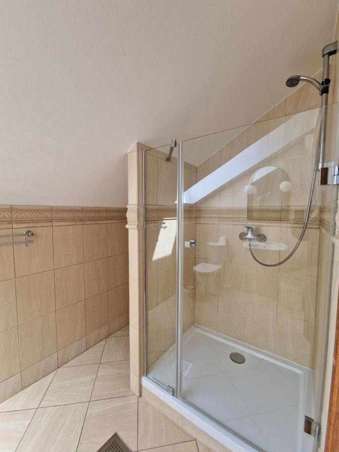 Jasna łazienka z kabiną prysznicową z przezroczystego szkła, beżowe płytki z dekoracyjnym pasem, ukośny sufit.