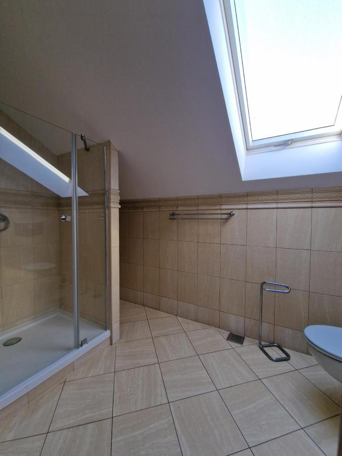 Jasna łazienka na poddaszu z kabiną prysznicową, beżowymi płytkami i oknem dachowym.