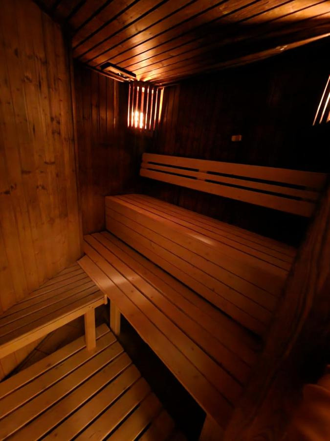Wnętrze sauny z drewnianymi ławkami oświetlonymi ciepłym, pomarańczowym światłem.