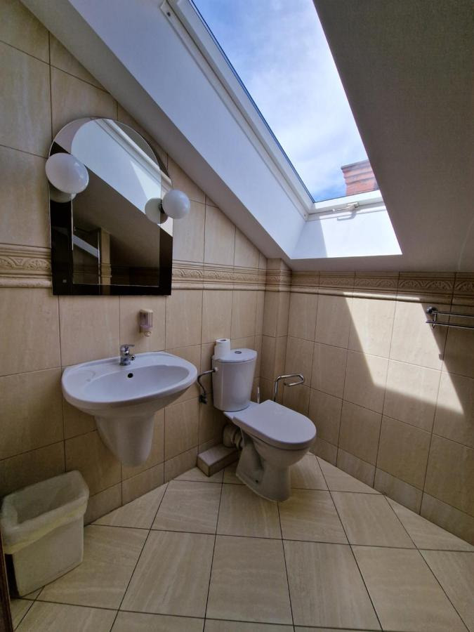 Jasna łazienka na poddaszu z oknem dachowym, beżowe płytki na ścianach i podłodze, umywalka z lustrem i toaleta.