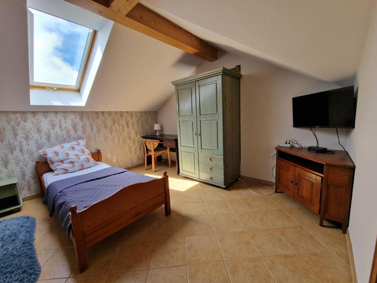 Pokój na poddaszu z drewnianym łóżkiem, szafą w kolorze pistacjowym, biurkiem i telewizorem na szafce z brązowego drewna, oświetlony przez okno dachowe.