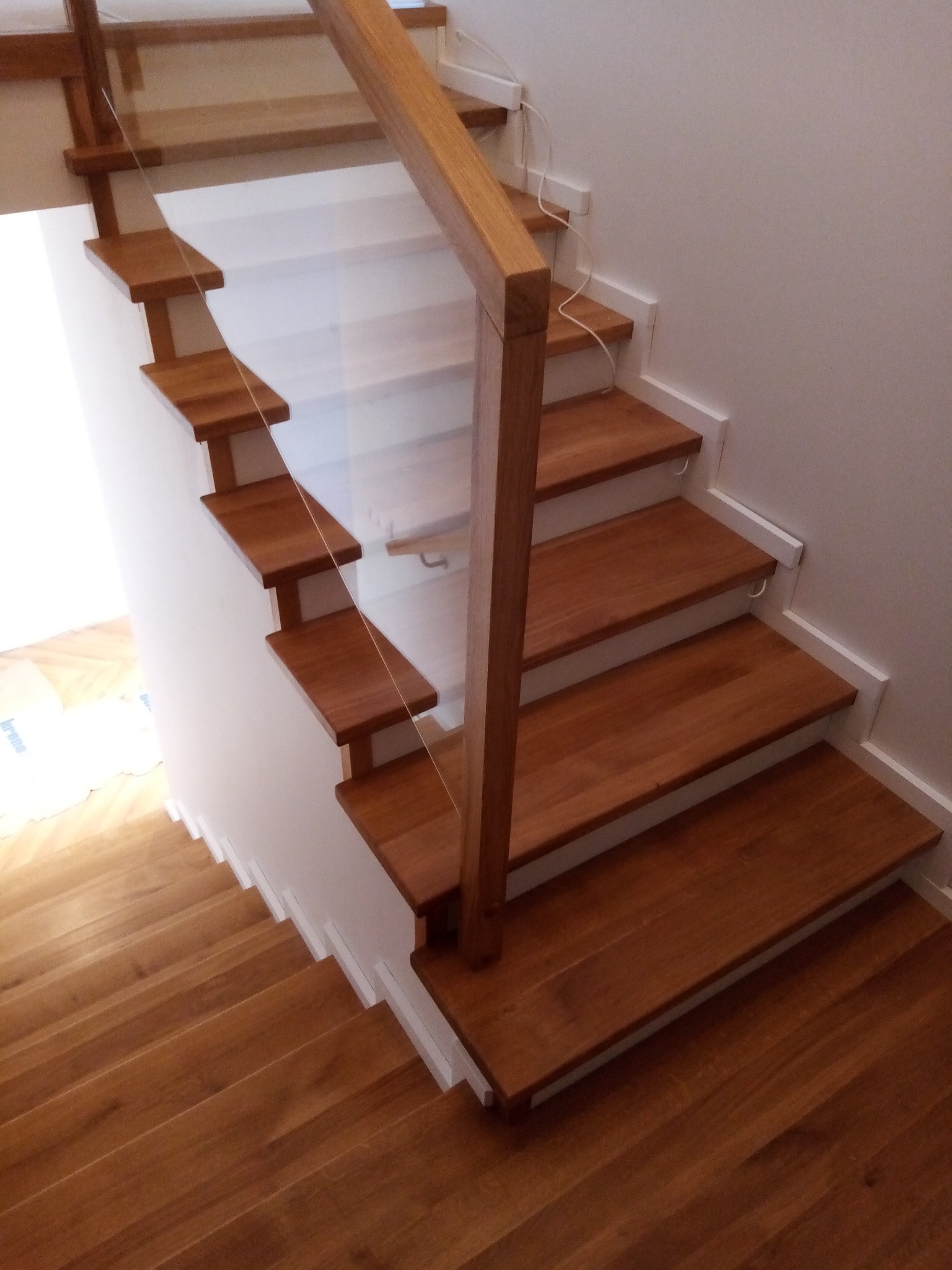 Nowoczesne schody z drewnianymi stopniami i szklaną balustradą, widok z góry, minimalistyczny design.