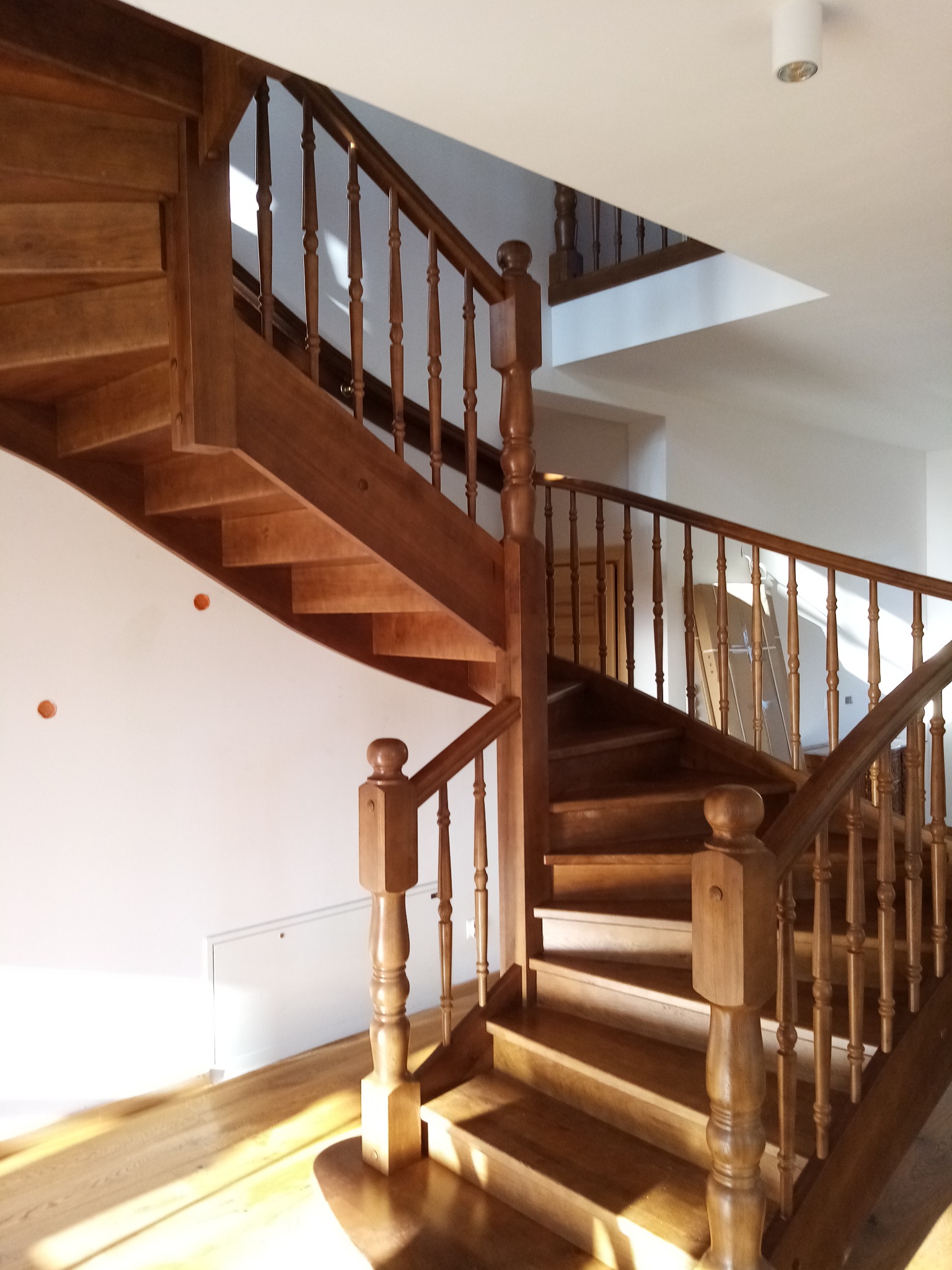 Wewnętrzne, drewniane schody spiralne z balustradą o toczonych tralkach, widoczne otwory montażowe w ścianie i kartony w tle.