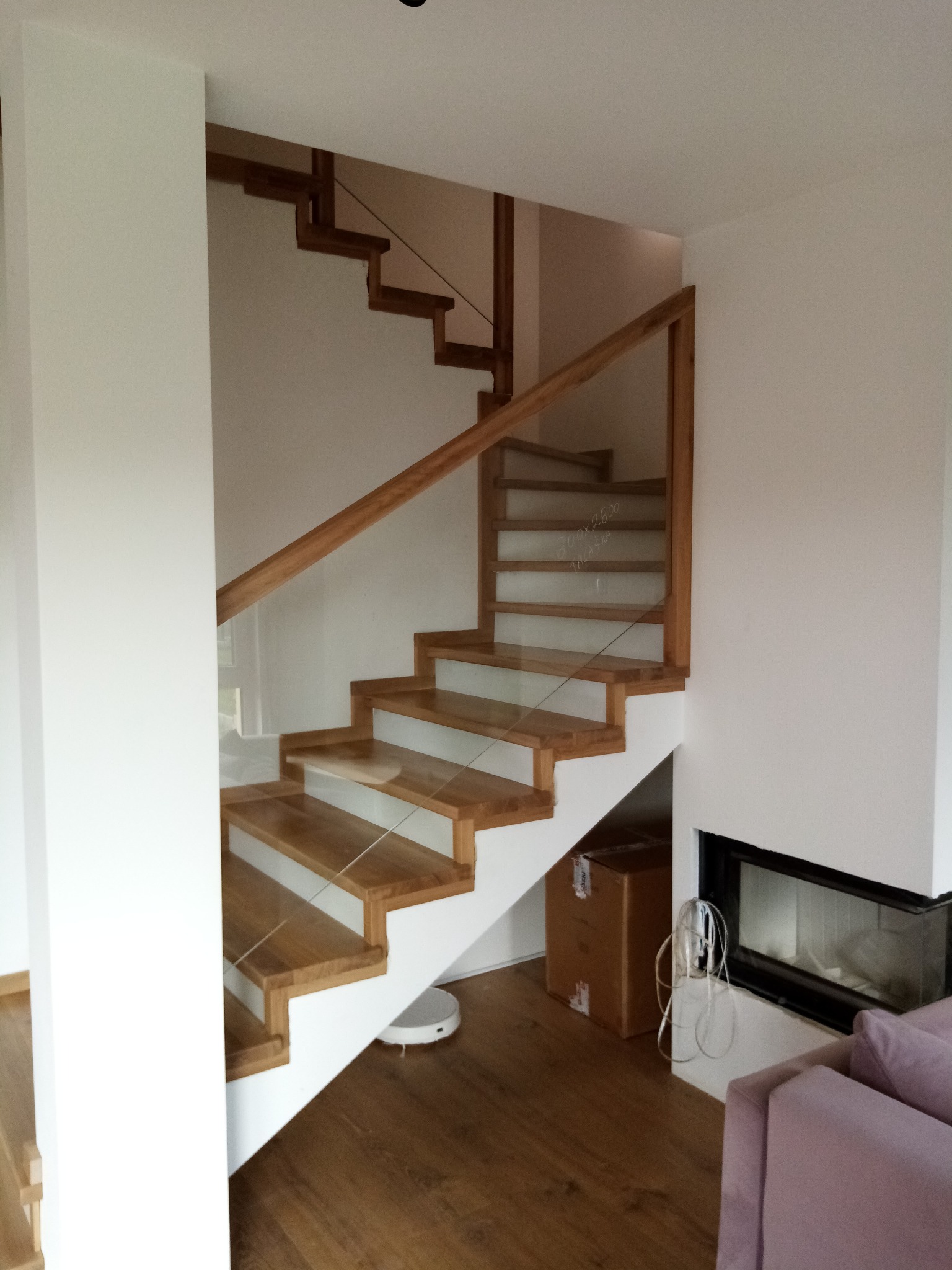 Nowoczesne schody z drewnianymi stopniami i szklanymi balustradami w jasnym wnętrzu z kominkiem.