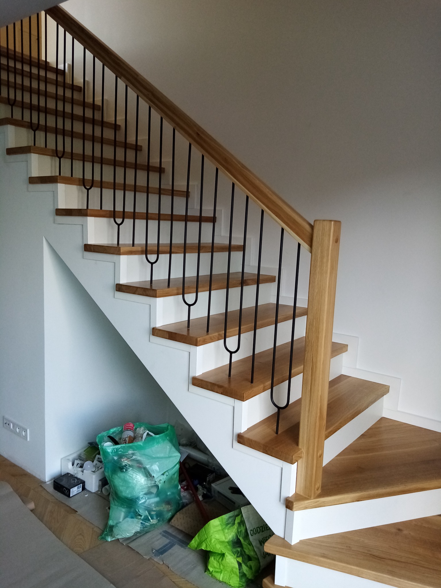 Nowoczesne schody z drewnianymi stopniami i czarnymi, metalowymi balustradami w trakcie montażu, widoczne śmieci budowlane i zabezpieczenia podłogi.