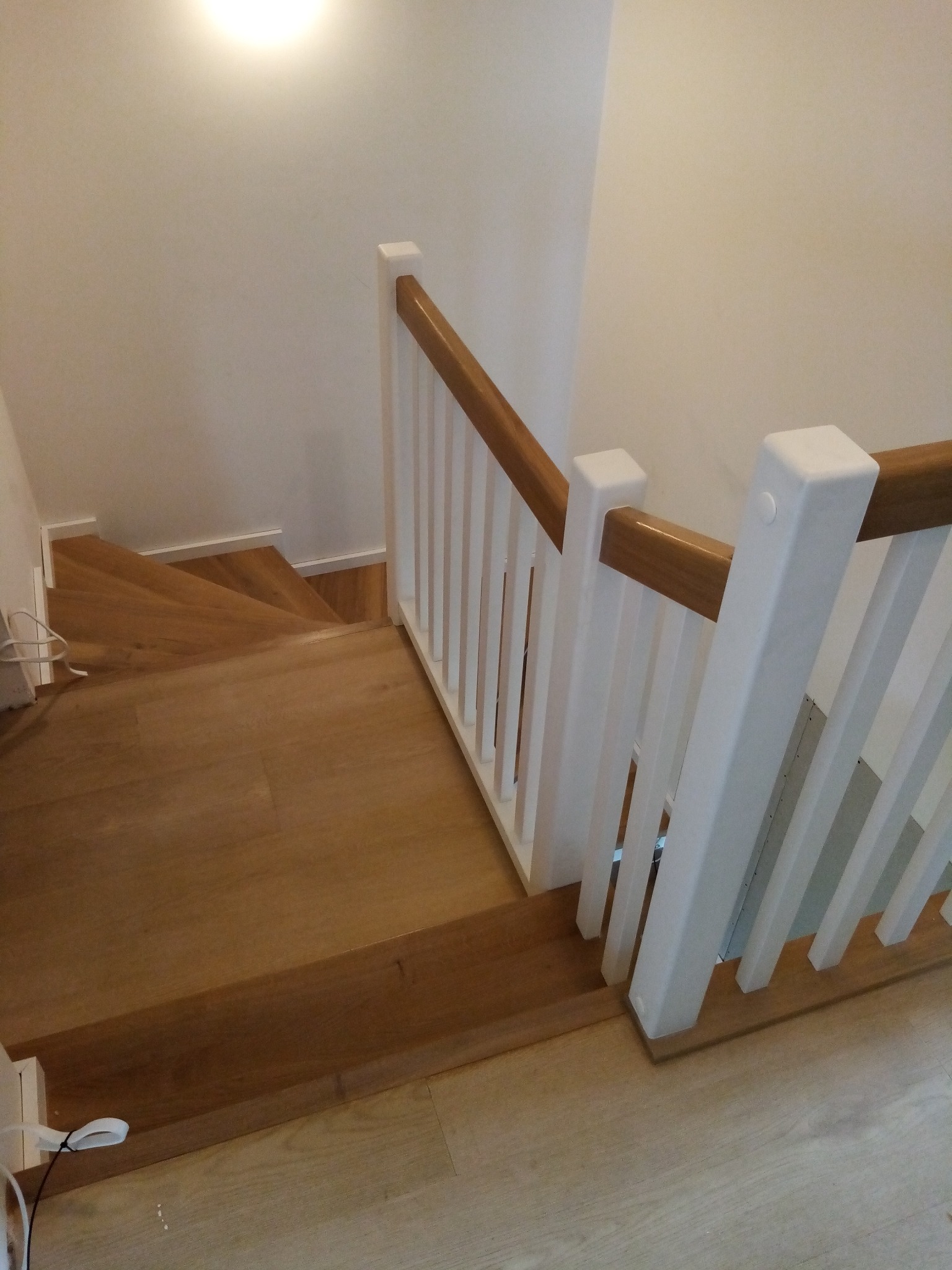 Widok z góry na dębowe stopnie z białymi pionowymi balustradami i drewnianą poręczą, oświetlone światłem z góry.
