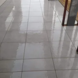 Świeżo ułożona, jasnoszara, błyszcząca nawierzchnia z płytek na zewnątrz budynku, widoczne słupy konstrukcyjne i przygotowany teren w tle.