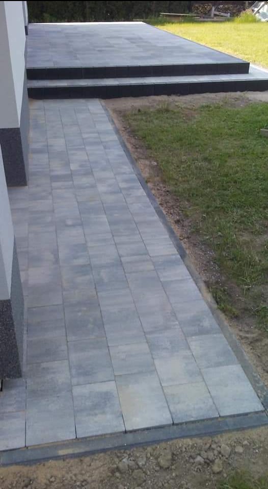 Szara kostka brukowa ułożona jako chodnik i taras z dwoma stopniami, widok z góry, trawnik po prawej stronie.