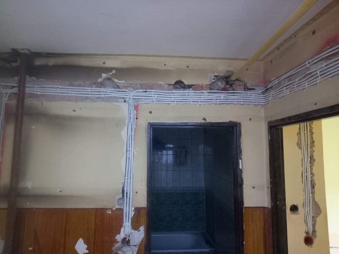 Białe przewody ułożone w rzędach na ścianie podczas remontu łazienki, widoczne fragmenty odsłoniętej cegły i uszkodzonego tynku.