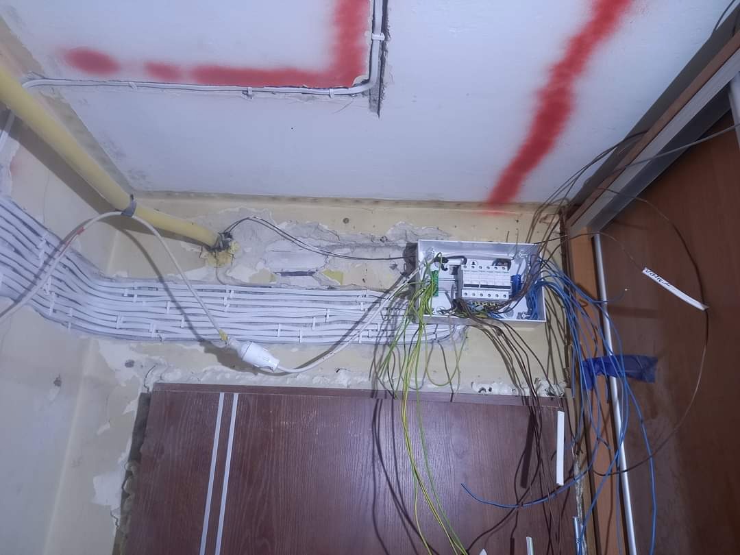 Rozdzielnica elektryczna w trakcie montażu z widocznymi przewodami, rurami instalacyjnymi i śladami po malowaniu na suficie.