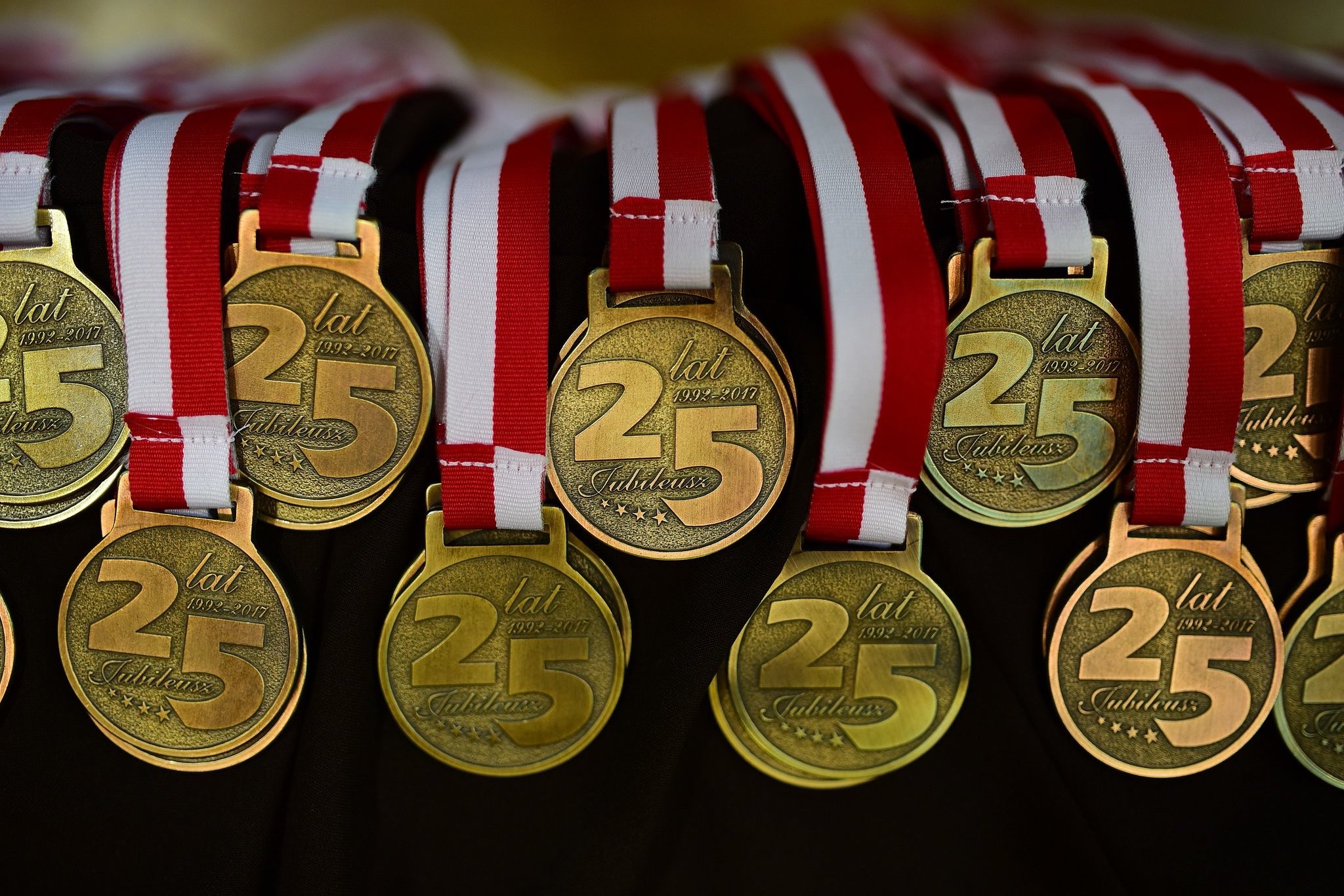 Złote medale z napisem '25 lat Jubileusz' zawieszone na czerwono-białych wstążkach, symbolizujące rocznicę lub jubileusz firmy.
