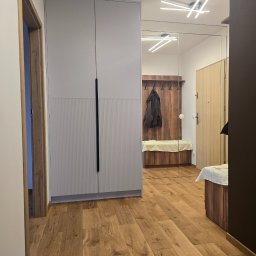 Meble Owczarek - Szafa wnękowa z lustrzanymi drzwiami, zintegrowana z aranżacją przedpokoju. Widoczne drewniane podłogi i nowoczesne oświetlenie sufitowe.