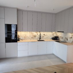 Meble Owczarek - Nowoczesna kuchnia z szarymi szafkami górnymi i białymi dolnymi, marmurowym blatem i czarną armaturą. Widoczne sprzęty AGD i oświetlenie podszafkowe.