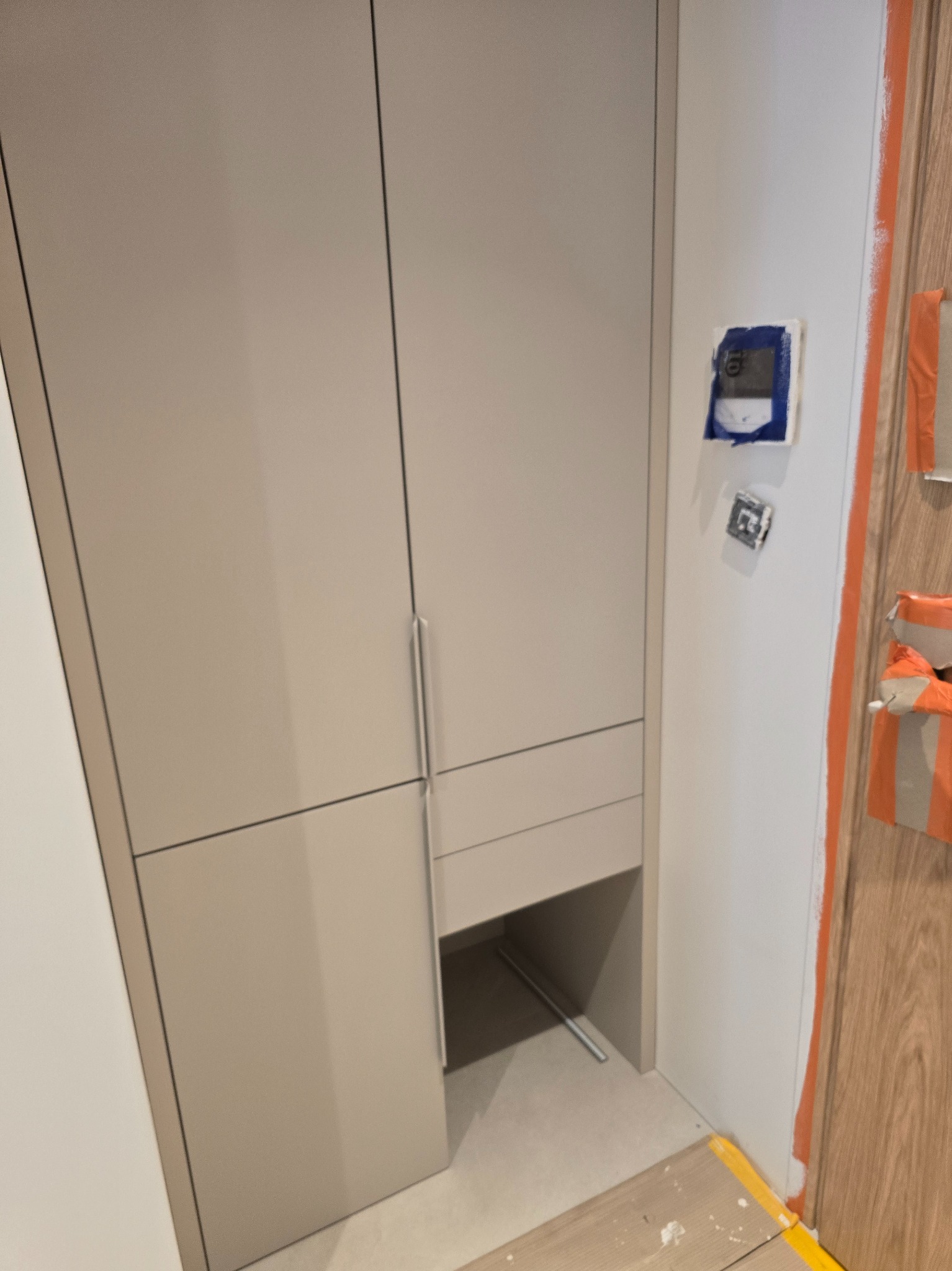 Jasna szafa wnękowa z szufladą i otwartą półką, minimalistyczny design, widoczne detale wykończenia i regulowany termostat na ścianie.