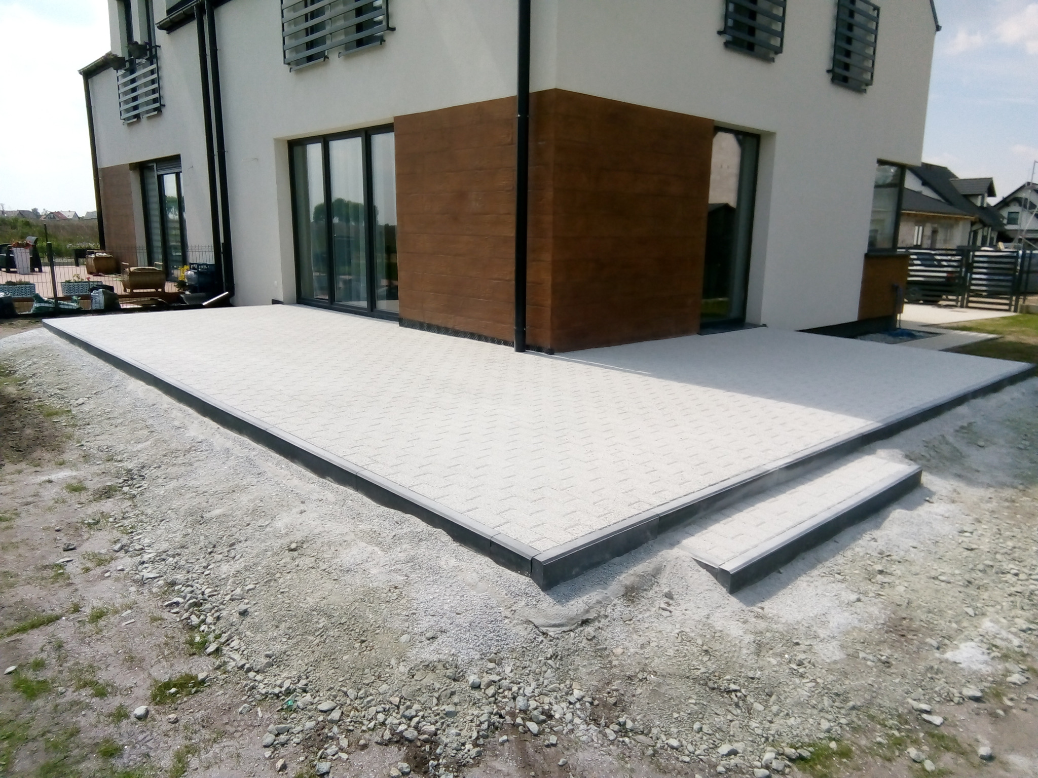 Taras z zejściem na ogród z kostki betonowej dekoracyjnej.