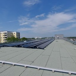 Energimixxxduo. S.c - Widok z góry na płaski dach budynku z zainstalowanymi panelami fotowoltaicznymi i systemem odgromowym, w tle budynki mieszkalne i żuraw budowlany.