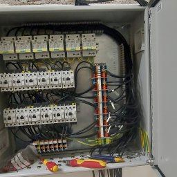 Energimixxxduo. S.c - Otwarta skrzynka rozdzielcza z zainstalowanymi bezpiecznikami, stycznikami i listwami zaciskowymi, widoczne przewody oraz narzędzia: śrubokręty i szczypce.