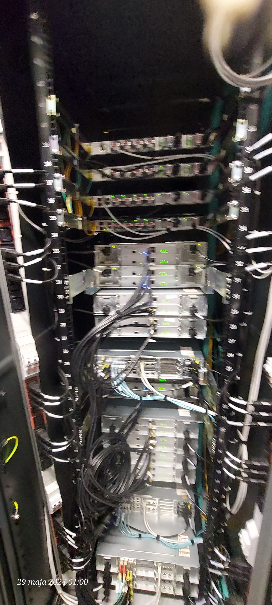 Widok z góry na szafę rack z serwerami i okablowaniem, widoczne liczne przewody i światła kontrolne urządzeń.