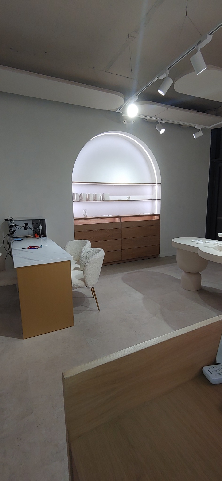 Jasne wnętrze sklepu z minimalistycznym wystrojem, drewnianymi meblami i oświetloną wnęką ekspozycyjną w kształcie łuku.