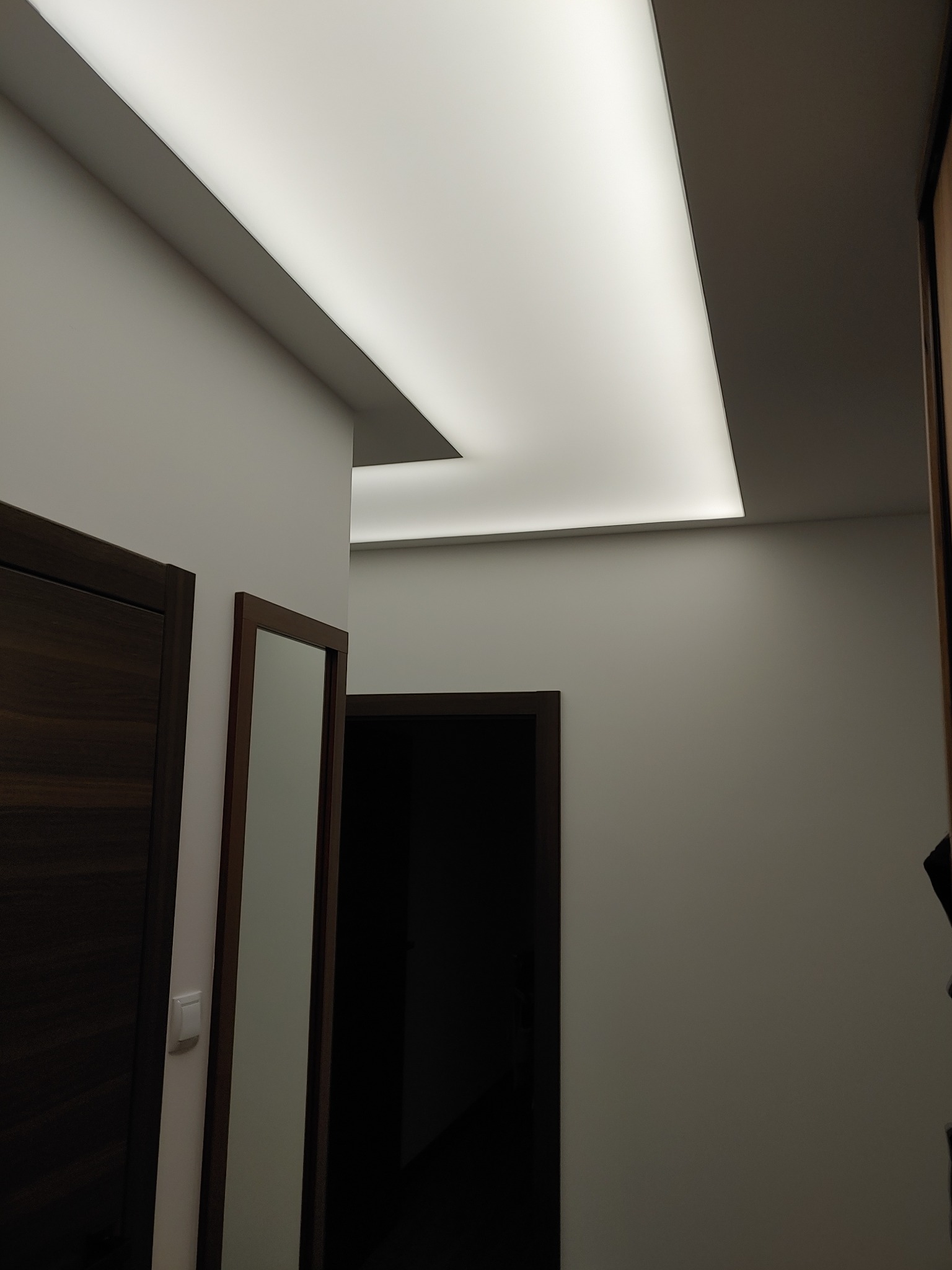 Nowoczesne oświetlenie sufitowe LED w korytarzu z drzwiami i lustrem w ramie.