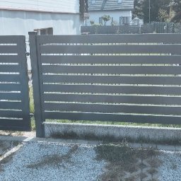 Kamil Nowak Ogrodzenia - Nowoczesne, poziome ogrodzenie panelowe w kolorze antracytowym z furtką, zamontowane na posesji z widocznym trawnikiem i domem w tle.