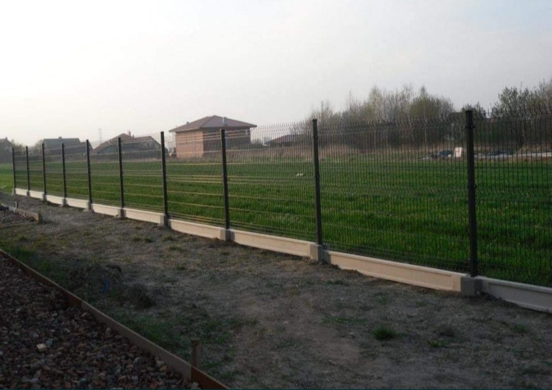 Nowo zamontowane ogrodzenie panelowe z podmurówką betonową na tle zielonej trawy i zabudowań.