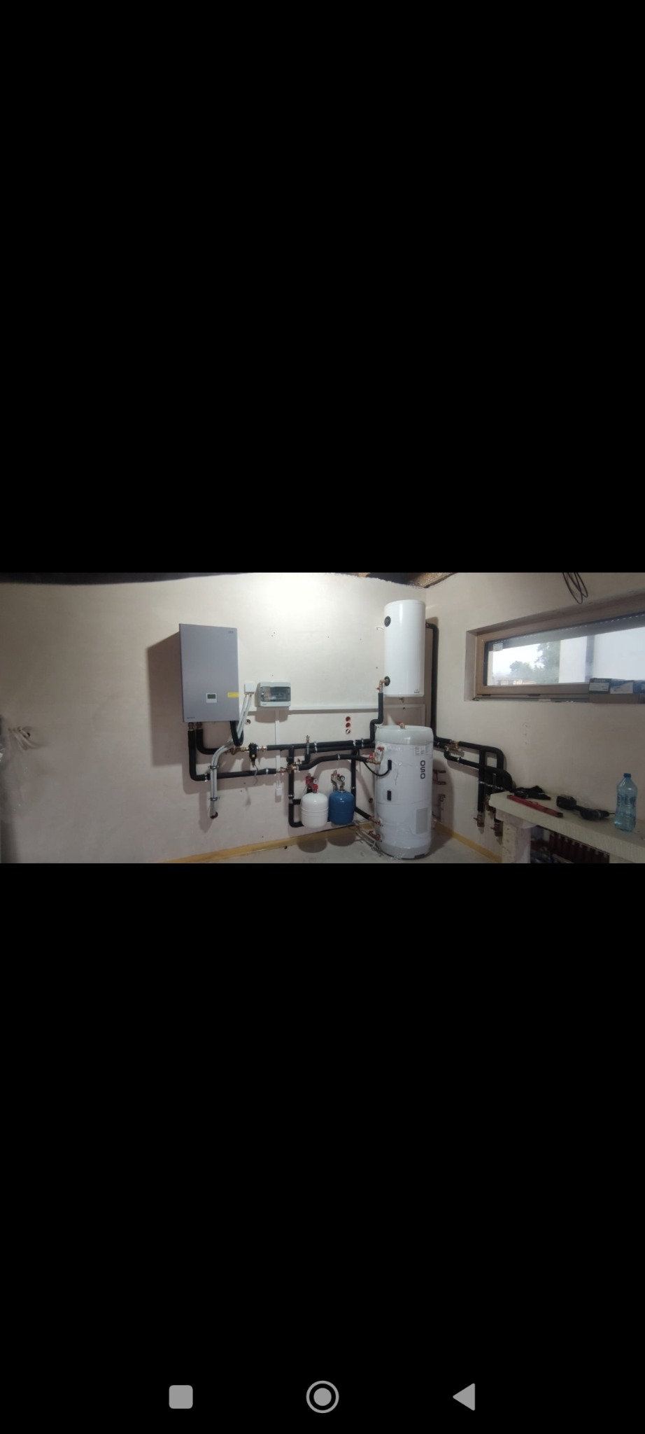 Złożona instalacja grzewcza z kotłem, zasobnikiem i rurami w piwnicy. Widoczne elementy montażowe i podłączenia. Świeżo po instalacji, gotowa do użytku.