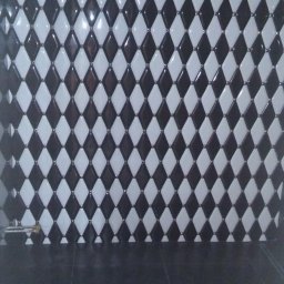 Igor Martsynkovskyi - Ściana wyłożona błyszczącymi, romboidalnymi płytkami w szachownicę czarno-białą, z ciemną podłogą i widoczną żarówką na kablu u góry.