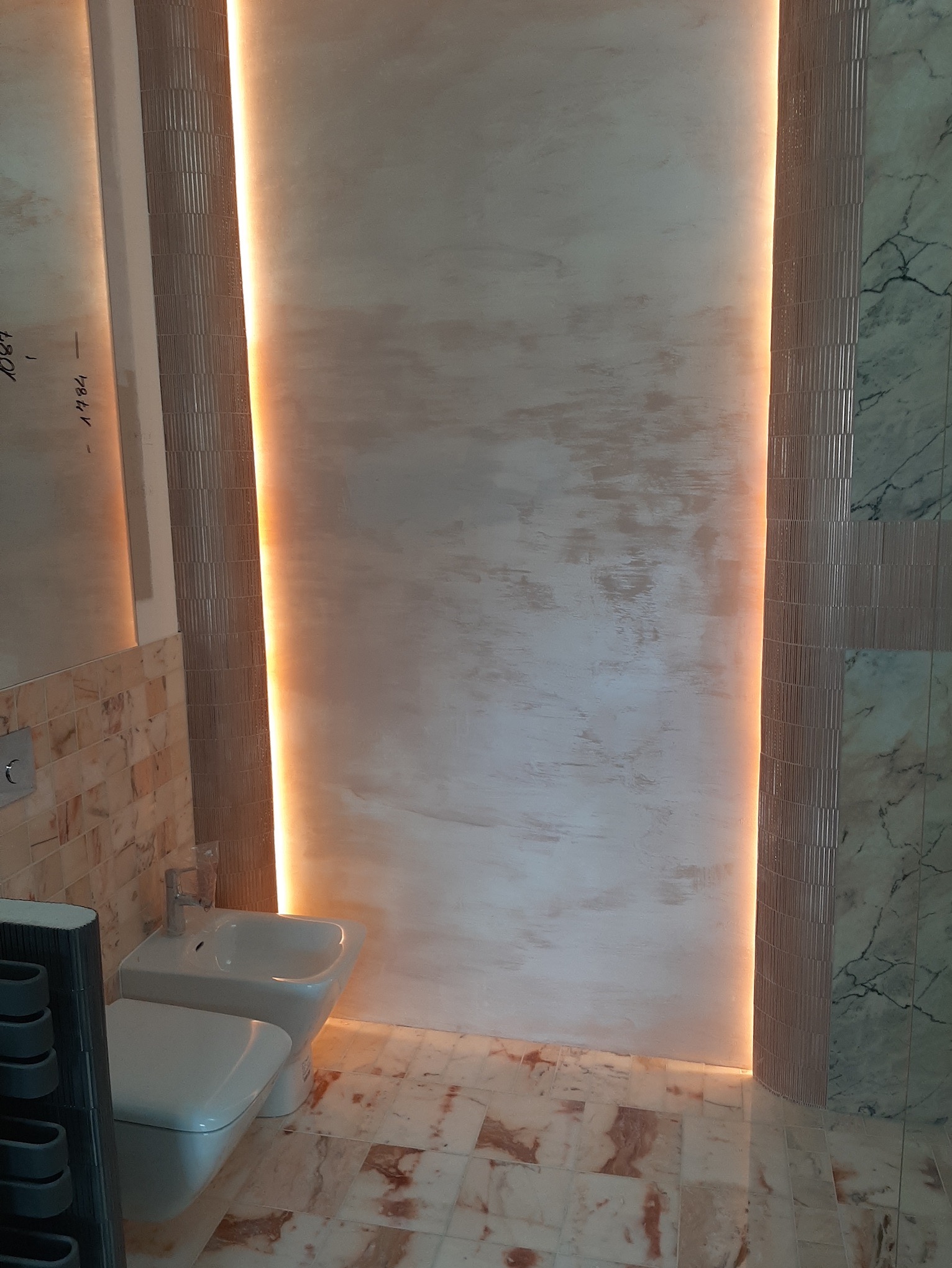 Wykończona łazienka w Warszawie z podświetlanymi panelami ściennymi po bokach, marmurowymi płytkami podłogowymi i częściowo na ścianach oraz białą toaletą i bidetem.