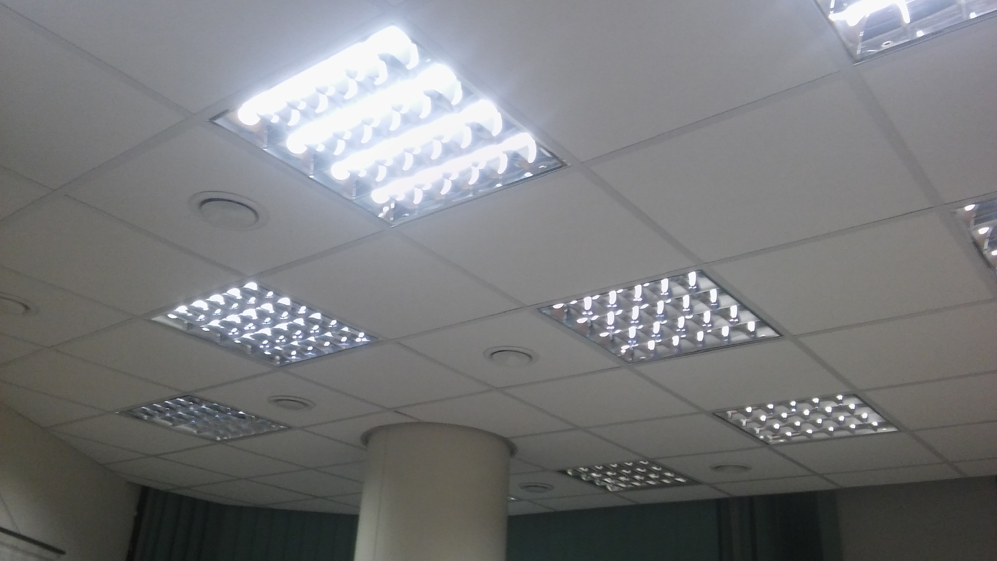 Sufit podwieszany z kwadratowymi panelami i wbudowanym oświetleniem rastrowym, widoczny fragment kolumny nośnej.