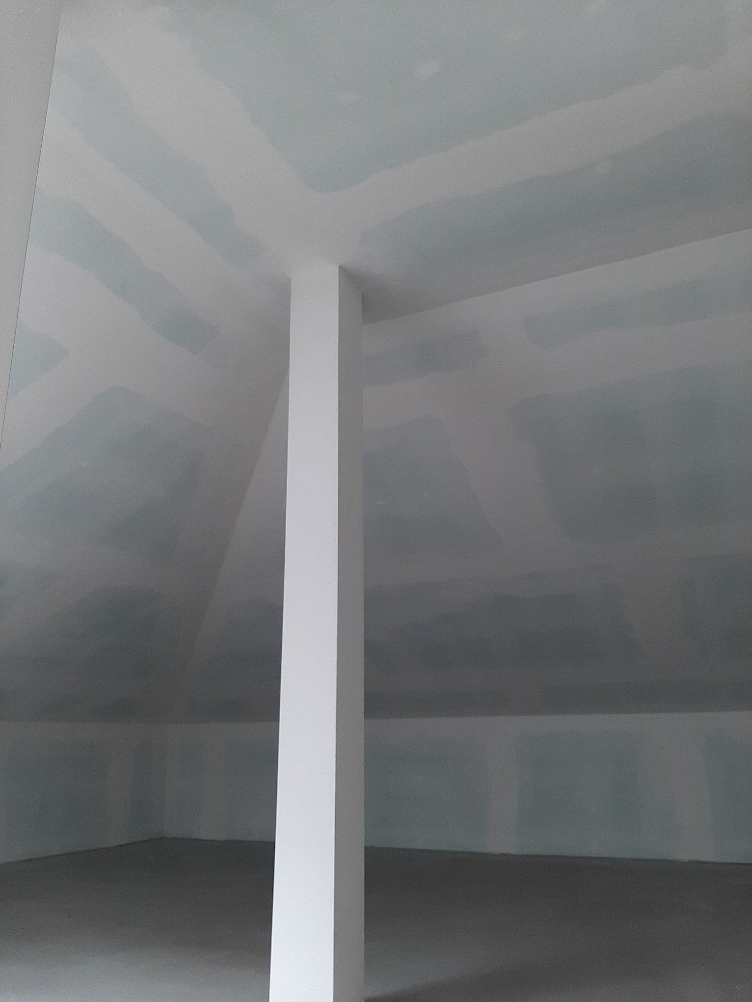 Poddasze z ukośnym sufitem pokrytym płytami kartonowo-gipsowymi, widoczne łączenia płyt przed szpachlowaniem, pionowa kolumna konstrukcyjna w centrum kadru.