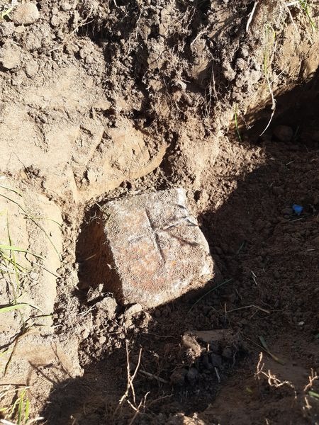 Odkopany w ziemi kamienny znak graniczny z wyrytym krzyżem, oznaczający punkt osnowy geodezyjnej.