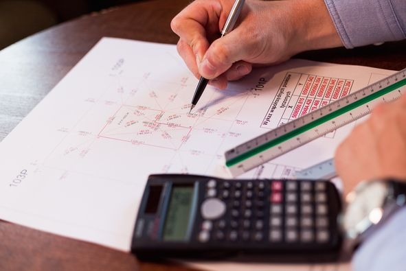 Geodeta nanosi poprawki na mapę działki za pomocą cienkopisu, obok kalkulator, skala i tabela współrzędnych.