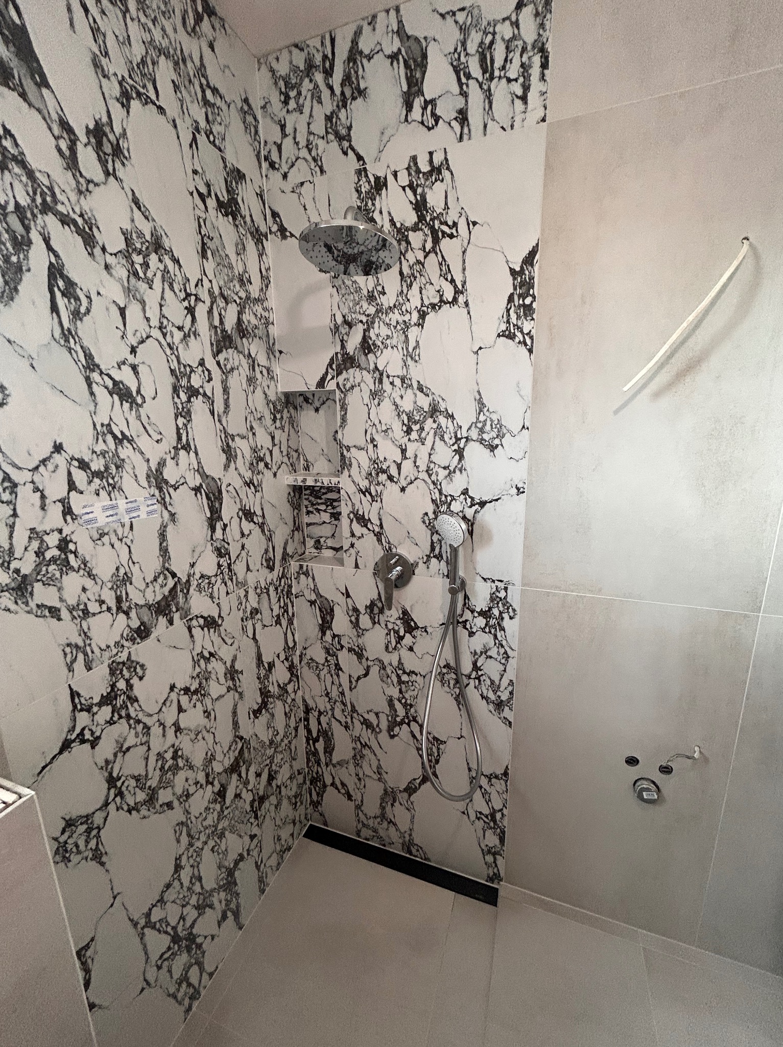 Kabina prysznicowa z marmurowymi płytkami, chromowaną armaturą i wnęką na kosmetyki. Kontrastowe wykończenie, nowoczesny design.