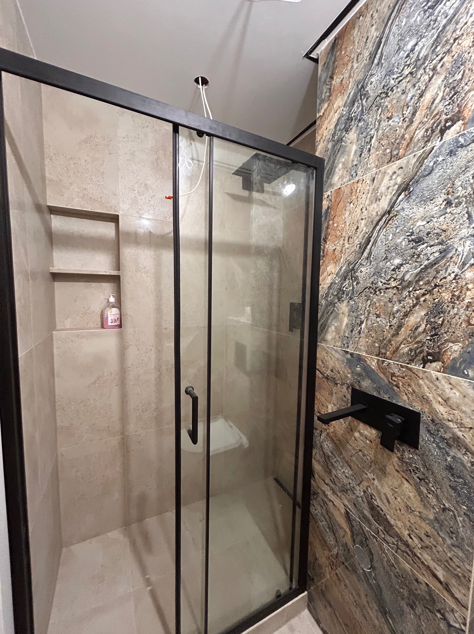 Kabina prysznicowa z czarną ramą i marmurową ścianą w Małopolu. Widoczna półka wewnątrz i nowoczesna bateria.