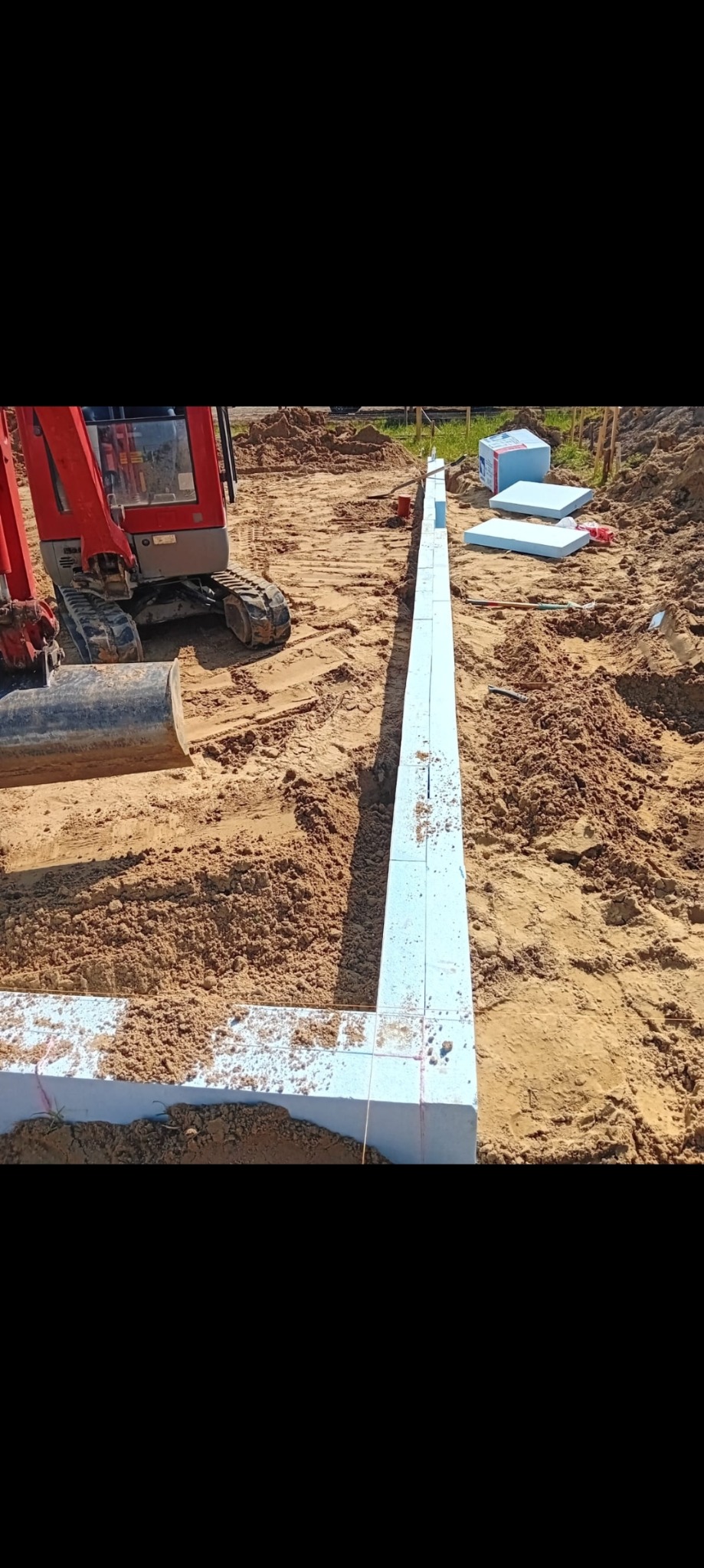 Przygotowanie wykopu pod fundamenty: widoczna mini koparka, ułożone płyty izolacyjne z polistyrenu ekstrudowanego tworzące szalunek, ziemia wokół wykopu.