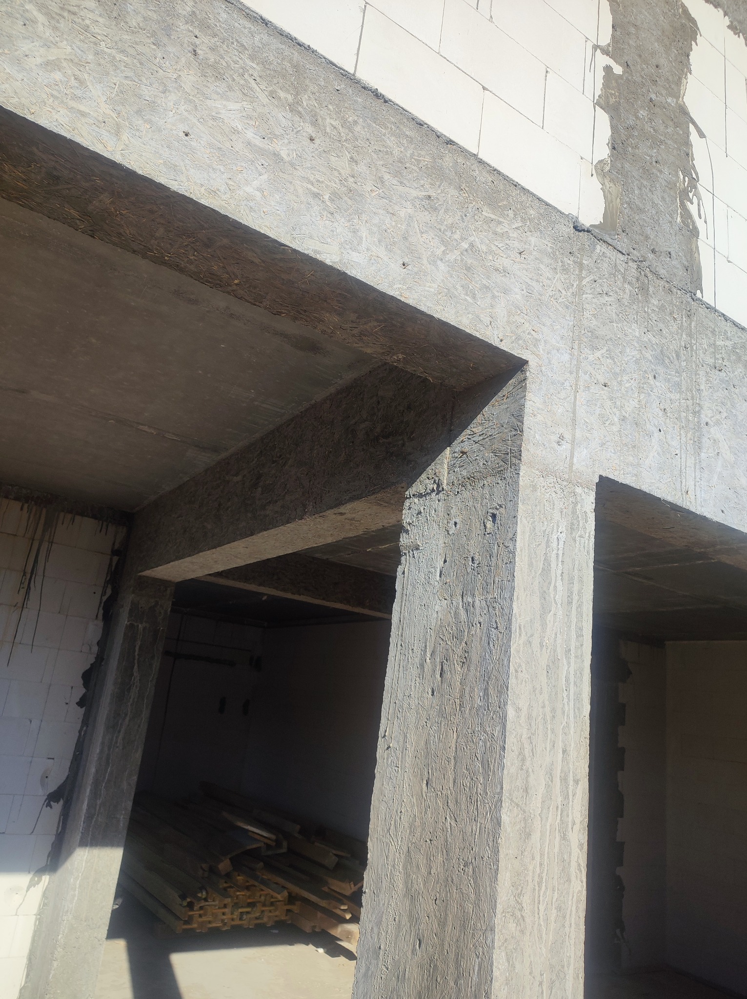 Surowy stan domu w budowie we Wrocławiu, widoczne ściany z betonu komórkowego i szalunki stropowe z płyty OSB, w tle składowane drewniane elementy konstrukcyjne.